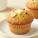 Freshly baked banana oatmeal muffins on a wooden table with a napkin and bananas in the background.