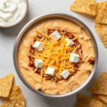 A crockpot filled with creamy Buffalo chicken dip topped with melted cheese and chopped green onions, served with tortilla chips.