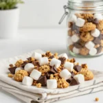 A bowl of S'mores trail mix with chocolate chips, mini marshmallows, graham cracker pieces, and nuts on a wooden table